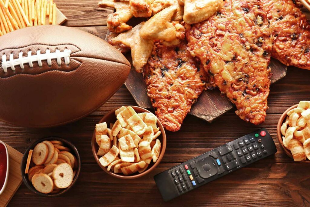 a bunch of snacks with a football and remote for the super bowl